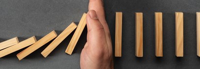 A hand blocking a row of domino's from falling in the middle